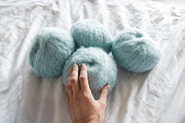 Woman's hand touches skeins of alpaca wool on a white woven background