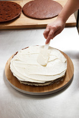 Woman is preparing chocolate cake with milk cream. The process of making the chocolate cake, from begin to the end. Made by hands for confectionery.