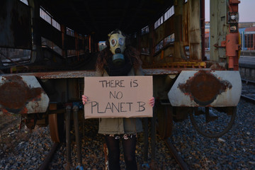 Girl with gas mask in an apocalyptic landscape and with a banner that says: there is no planet b....
