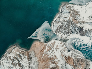 Aerial view of glacier patterns in lake. Glacial lagoon with ice floes. Climate change, global warming, melting glacier. Drone view of dry mountains of the sand with erosion and snow. Place forces.