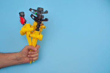 The male hand holds a supports rack for and a sprinklers on a blue background. Gardening equipment for watering.