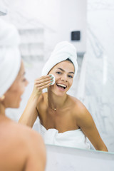 Focused beautiful young woman cleaning her skin with a cotton pad, looking at the mirror at home bathroom. Beauty, skin care concept, lifestyle