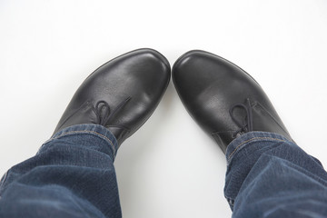 Men's legs in jeans and black classic shoes on white background