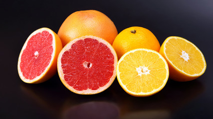 cut pieces of different citrus fruits on dark background