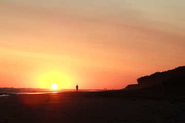 Fototapeta na wymiar una persona caminando por la playa al atardecer con el sol en el fondo