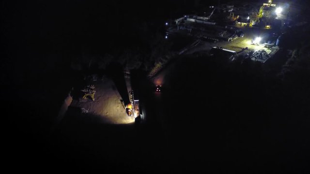 Aerial footage of a car driving alone in the middle of the night to a base camp of an onshore oil rig. The car arrives and enters the location.