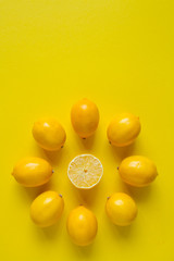 Top view whole and sliced ripe lemons laid out in the shape of a dial on a yellow surface, concept of health and vitamins