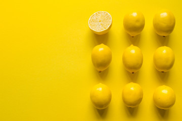 Top view whole and sliced ripe lemon laid out in several rows on a yellow surface, concept of health and vitamins