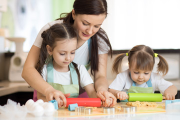 Fototapeta premium Adorable mother and her kids daughters cooking together in the kitchen