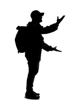 Silhouette of a man wearing a backpack looking like a traveler or hiker trekking.  He is gesturing like he is talking or speaking