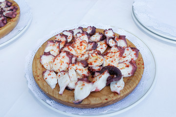  an octopus with boiled potatoes, typical Spanish Galician dish, on a traditional wooden plate on a teal background with copy space