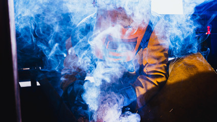 Hombre soldador a través del humo soldando metal