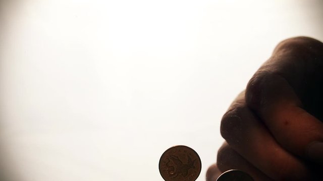 View from below as the hand throws gold coins. Moves them, collects them in the shape of a heart or columns.White background. Indoors.
