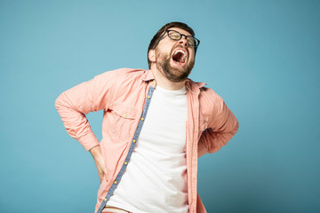 Naklejka premium Bearded man feels very severe pain in the lower back, he closed eyes from suffering, opened mouth wide and screams.