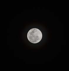 Bright white full moon in the night sky with solar rings in background