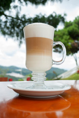 Glass cup served with Capuccino coffee, aromatic coffee from Guatemala served outdoors, relaxing and natural space.