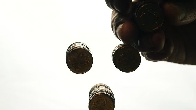 View from below as the hand throws gold coins. Moves them, collects them in the shape of a heart or columns.White background. Indoors.