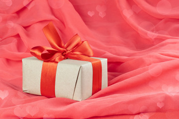 Gift box with red ribbon and bow on red silk background. Concept of minimal background for Valentine's day.