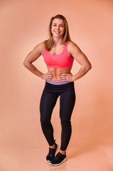 Vertical portrait of a pretty fitness blonde girl with a beautiful smile, excellent teeth and a bodybuilder figure in a tracksuit on a pink background. Cute looks at the camera, standing straight.