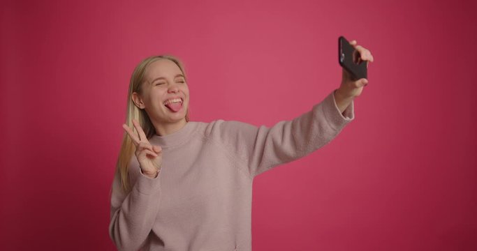 Beautiful blonde girl taking selfie with a smart phone at pink background
