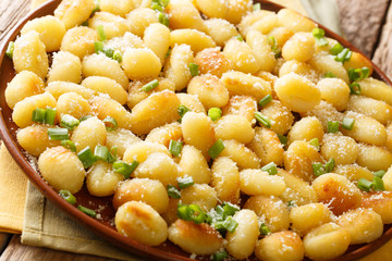 Tasty fried potato gnocchi with garlic sprinkled with parmesan and green onions close-up on a plate on the table. horizontal