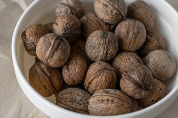 A white plate full of inshell walnuts stands on a brown background from crumpled old kraft paper. Top view flatlay