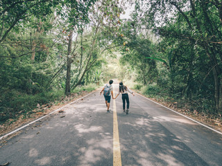 Traveler couple hold hands walking on forest road amid lush trees. Happy couple enjoying free time while traveling.