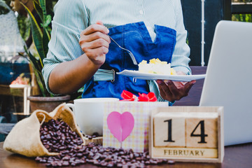 Business women eating cake after using laptop and drinking coffee with 14 February wooden calendar in Valentine day