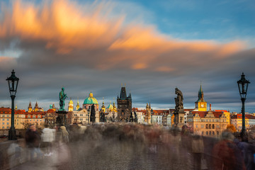 Prague, Czech Republic - Amazing golden sunset and moving clouds and huge crowd on the world famous Charles Bridge (Karluv most) with St. Francis of Assisi Church on a winter afternoon