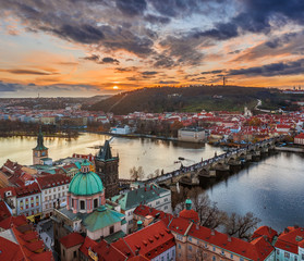 Prague, Czech Republic - Aerial panoramic drone view of the world famous Charles Bridge (Karluv most) and St. Francis Of Assisi Church with a spectacular winter sunset and Perlin Hill at background