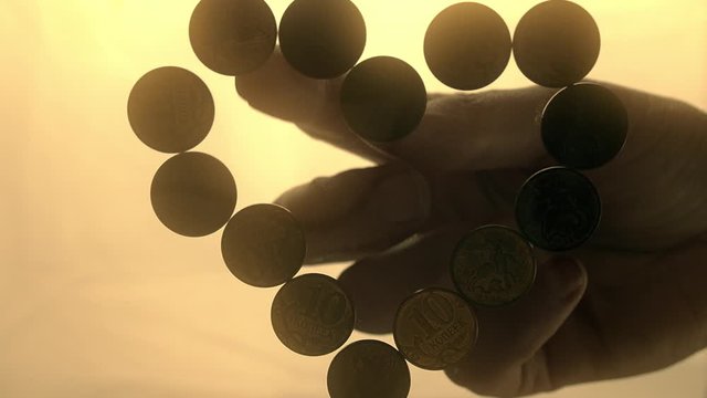 View from below as the hand throws gold coins. Moves them, collects them in the shape of a heart or columns.White background. Indoors.