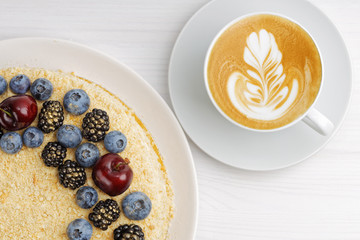 Cup of coffee cappuccino and homemade cake decorated with fresh berries on white wooden table. Top view