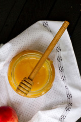 Yellow honey with fruit in a glass jar with a wooden spoon. sweet honey on a black wooden background. beekeeper. natural sweets. honey is lying on a dark table with peaches. health food.