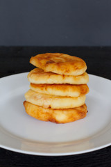 stack of pancakes on a black background. white plate with cheesecakes. breakfast.  the concept of the menu and cooking. five cheesecakes. delicious snack. pastry. space for text.