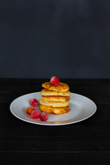  a stack of pancakes. pancake on a dark background with cherries. white plate with cheesecakes and berries on a black background. the concept of the menu and cooking. five cheesecakes. 