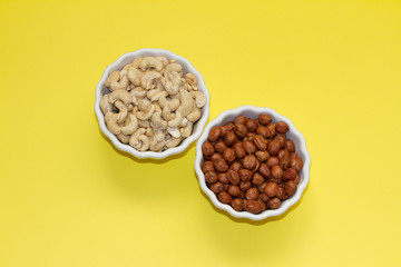 hazelnuts and walnuts in two white cups on a yellow background. lots of nuts. the concept of proper nutrition and health. Healthy food and snacks, organic vegetarian food. the view from the top. 