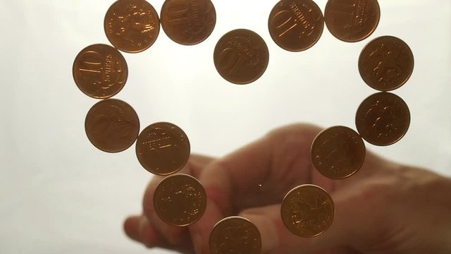 View from below as the hand throws gold coins. Moves them, collects them in the shape of a heart or columns.White background. Indoors.