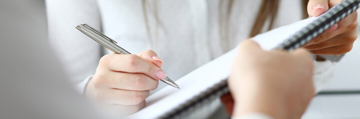 Close-up of people sitting in office and writing something in important document with tender female hands. Smart businessman holding paper folder. Blurred background