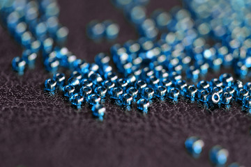 Transparent seed beads blue color scattered on a black leather surface close-up