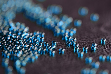 Transparent seed beads blue color scattered on a black leather surface close-up
