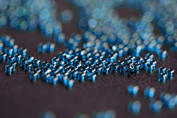 Transparent seed beads blue color scattered on a black leather surface close-up