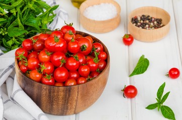 Ingredients for summer vegetable salad with cherry tomatoes, basil herb, olive oil and salt in on a wooden bowl white wooden background. Rustic style.