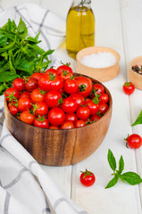 Ingredients for summer vegetable salad with cherry tomatoes, basil herb, olive oil and salt in on a wooden bowl white wooden background. Rustic style.