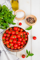 Ingredients for summer vegetable salad with cherry tomatoes, basil herb, olive oil and salt in on a wooden bowl white wooden background. Rustic style.
