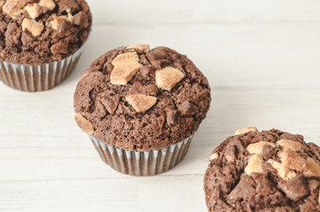 Three chocolate muffins lined up diagonally in white background.