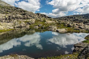 Fototapeta premium Lake landscape with clouds reflection, rocky mountain tundra, way to Trolltunga rock, Norway.