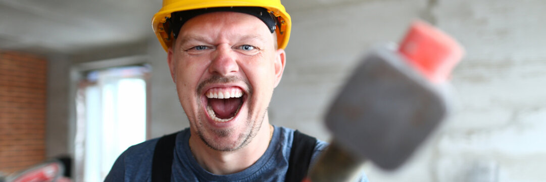 Portrait Of Screaming Male Holding Big Sturdy Construction Tool. Scary Builder Laughing At Camera With Joy And Madness. Strange Guy Wearing Yellow Hardhat And Bricklayer Outfit. Building Concept