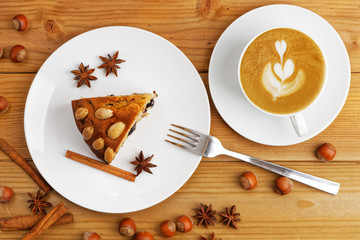 Piece of homemade cake with almonds and white cup of coffee cappuccino on a wooden table. Top view.
