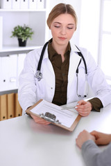 Young woman doctor and patient at medical examination in hospital office. Khaki colored blouse of therapist looks good. Medicine, healthcare and doctor's appointment concept