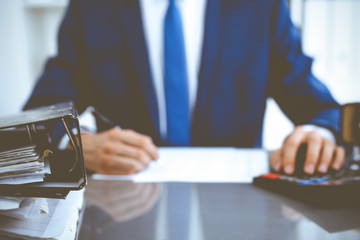 Binders with papers waiting to be processed with businessman or bookkeeper back in blur. Accounting...